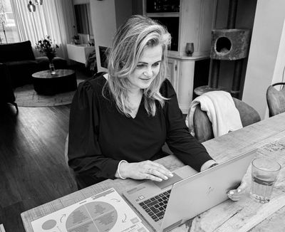 Vrouw die thuis op een laptop werkt, aan een houten tafel, met een document in de buurt.