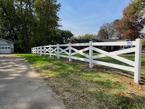A white fence is sitting on the side of a road next to a house.