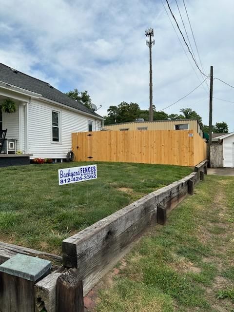 A wooden fence surrounds a lush green yard in front of a house.