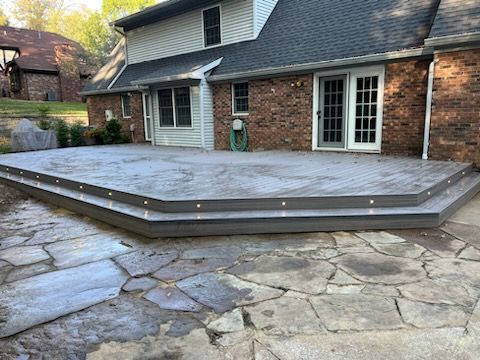 There is a large deck in front of a brick house.