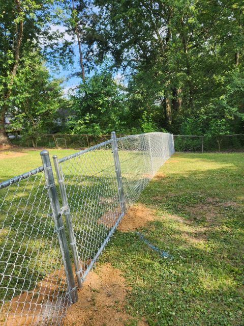 A chain link fence is sitting in the middle of a grassy field.