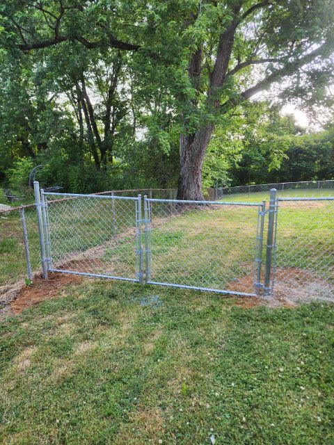 A chain link fence with a gate in the middle of a grassy field.