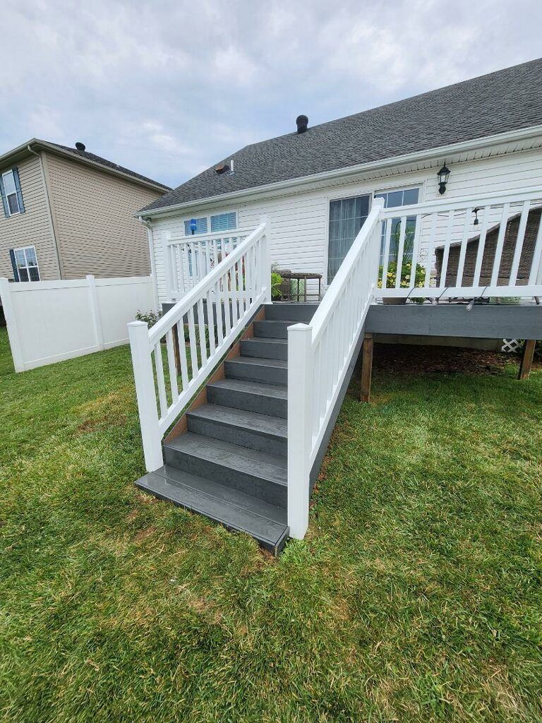 A white house with a deck and stairs leading up to it.