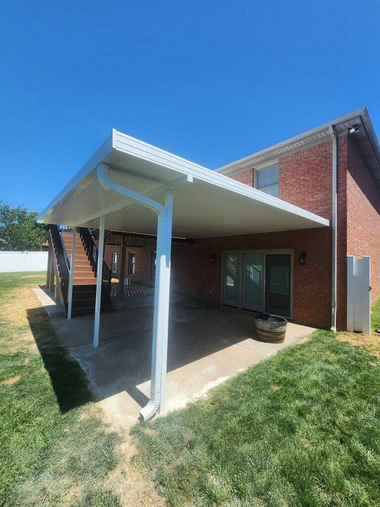 There is a covered patio in the backyard of a brick house.
