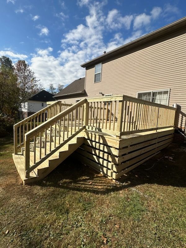 A wooden deck with stairs leading up to it is in the backyard of a house.