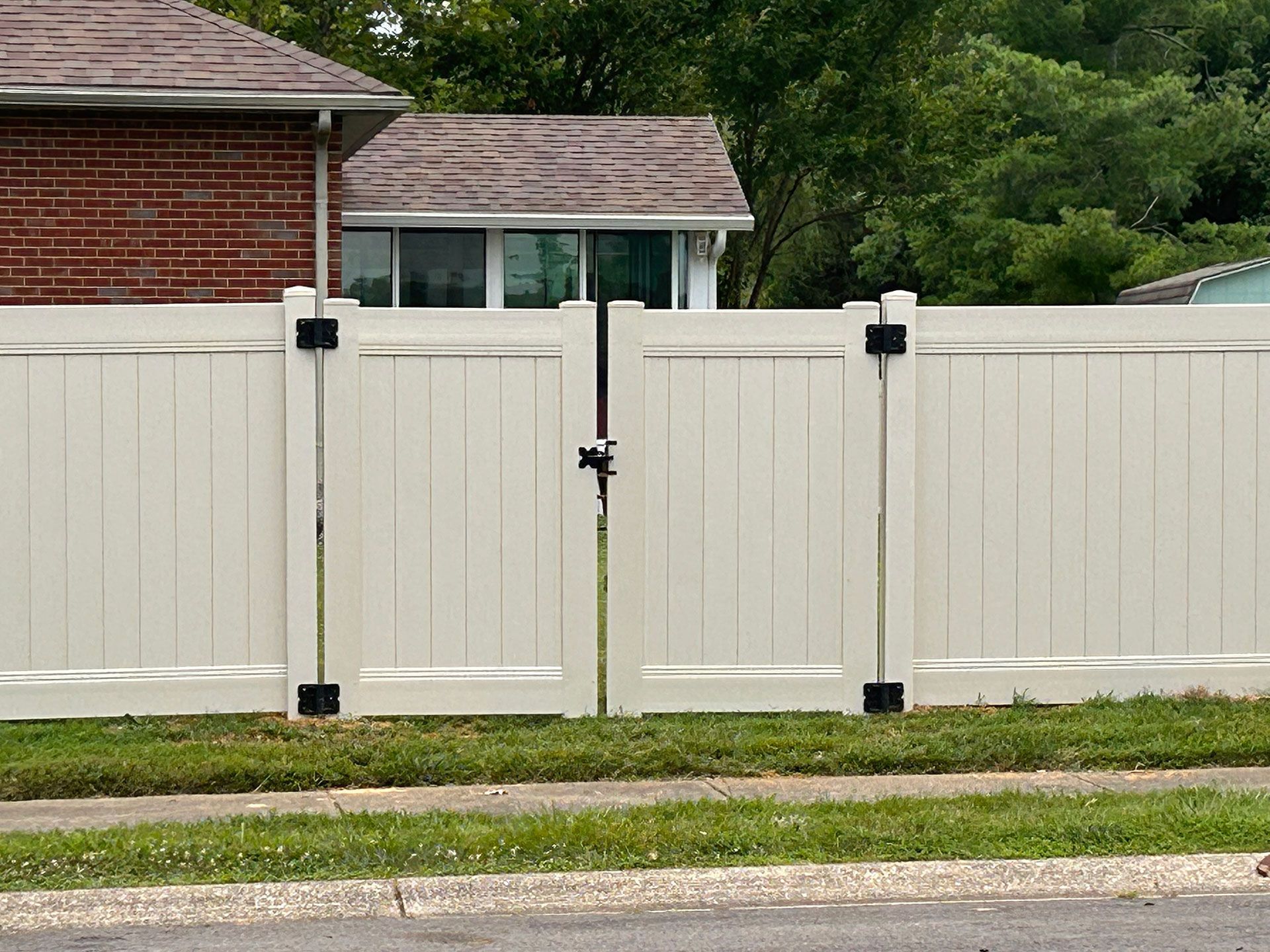 A white fence with a gate in front of a brick house.