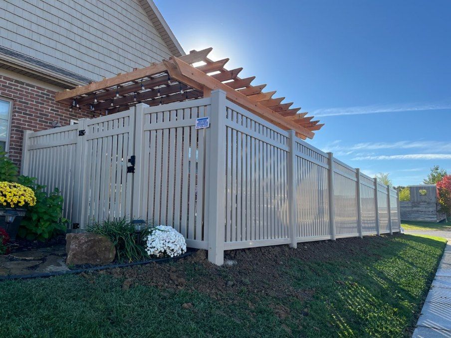A white fence with a pergola attached to it in front of a house.