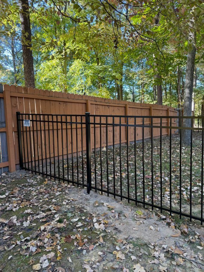 A black metal fence with a wooden fence behind it.