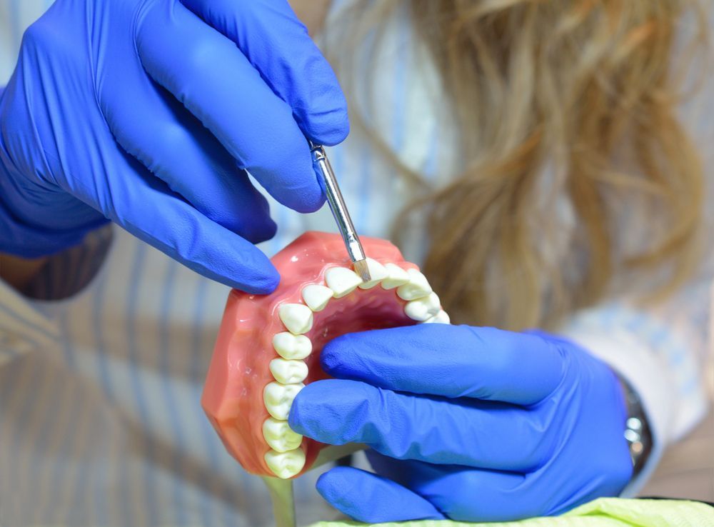 Persona con guanti blu che utilizza uno strumento odontoiatrico su un modello di denti.