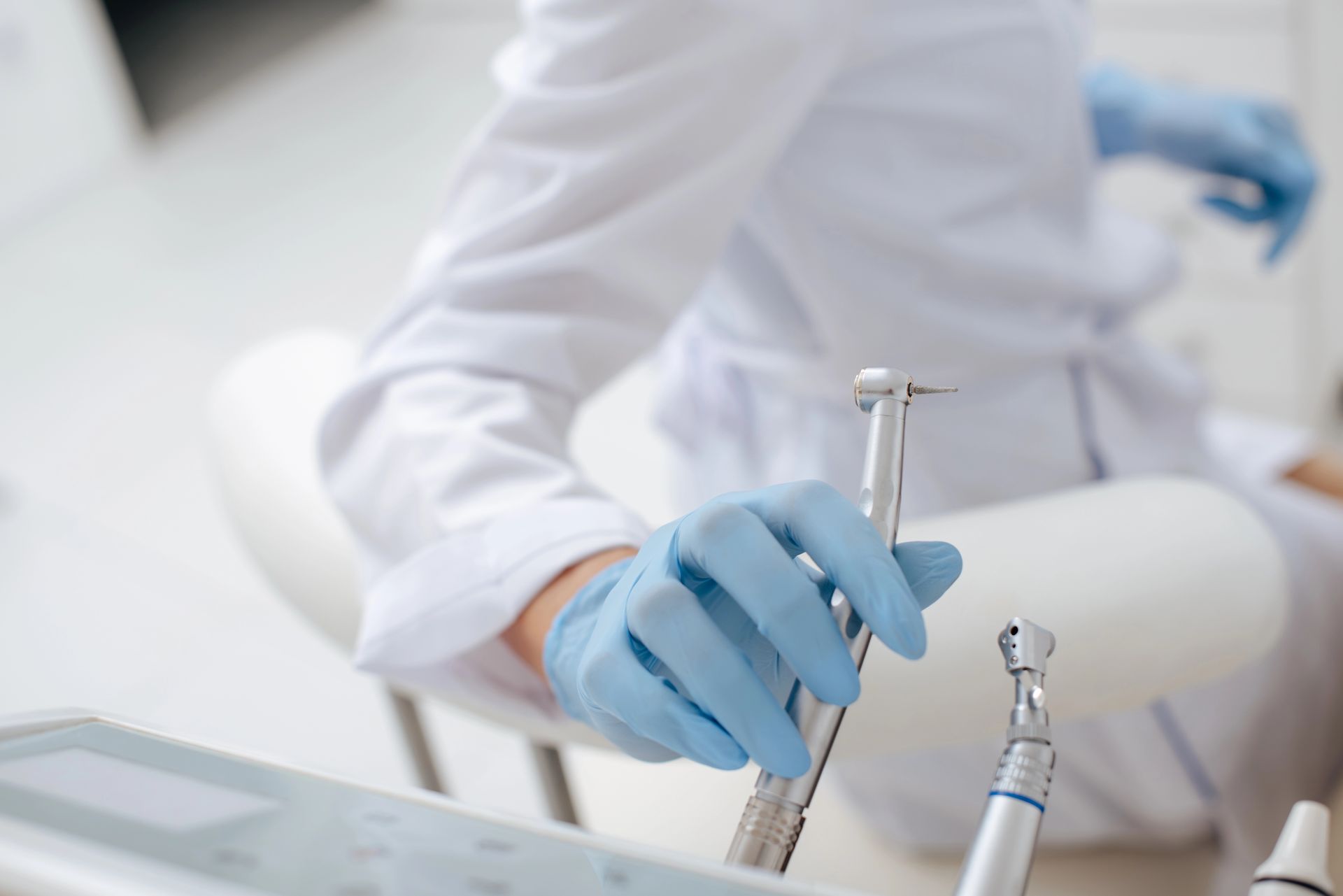 Dentista che indossa guanti blu e tiene in mano uno strumento odontoiatrico, mentre si prepara per la procedura.