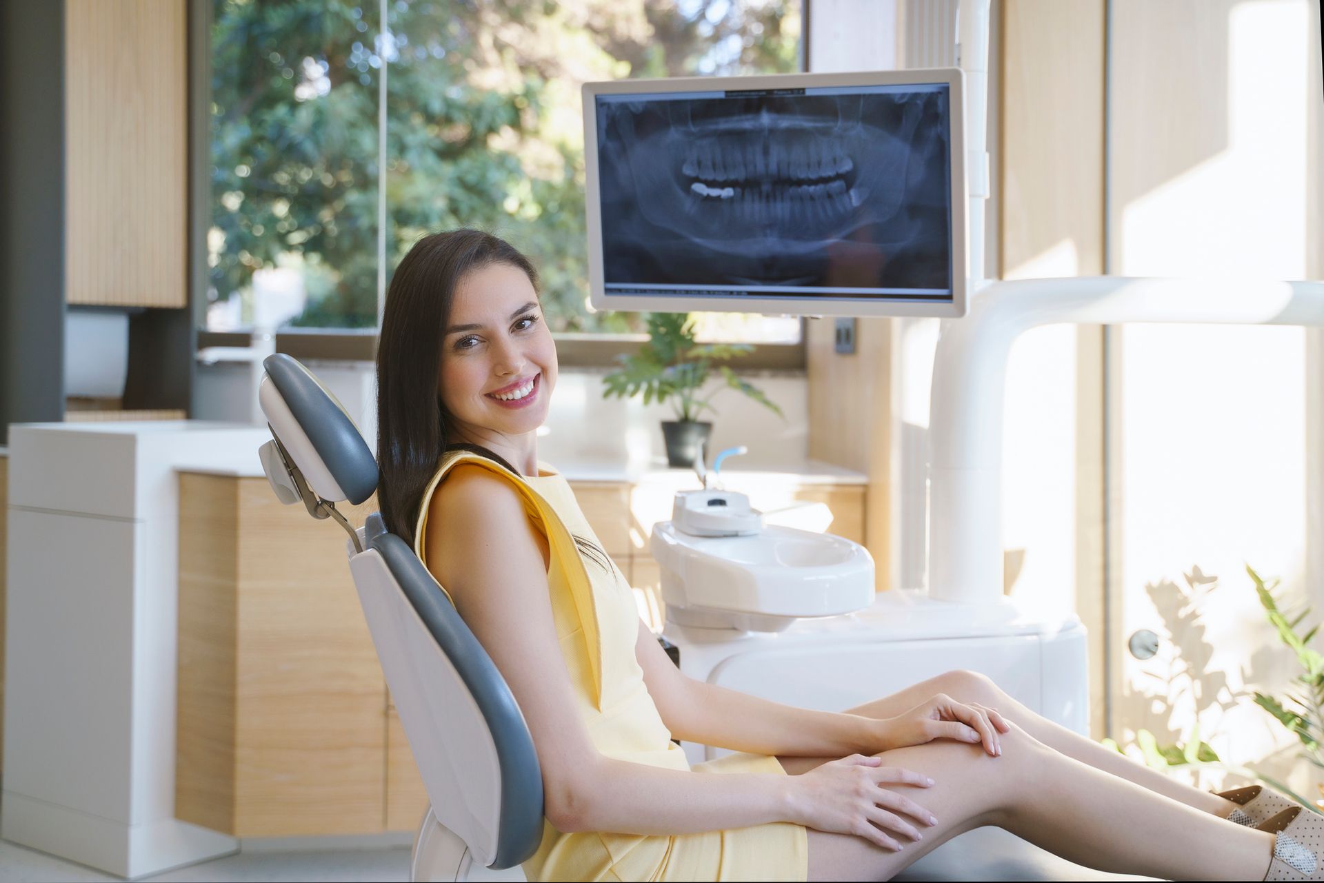 Una donna sorride seduta sulla poltrona del dentista, mentre una radiografia dentale viene visualizzata su un monitor.