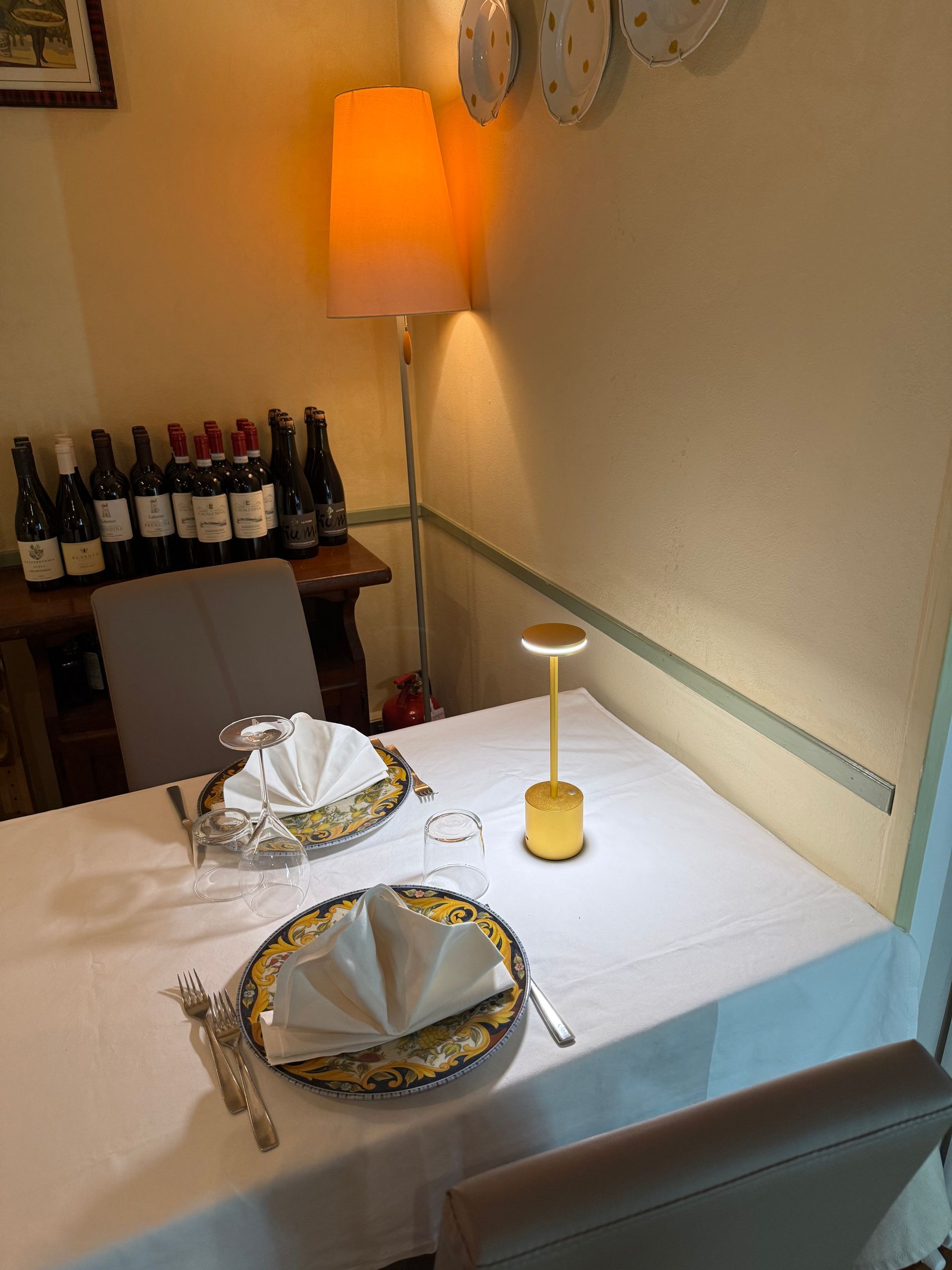 Un tavolo con piatti e utensili in una stanza con bottiglie di vino dietro.
