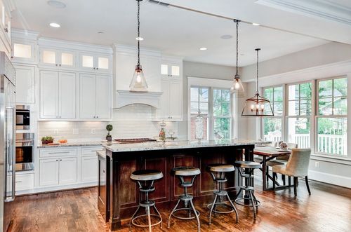 Bright modern kitchen with white cabinets, dark island, pendant lights, and bar stools by large windows