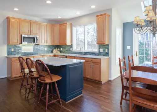 Bright kitchen with light wood cabinets, blue island, hardwood floors, and dining table by a window