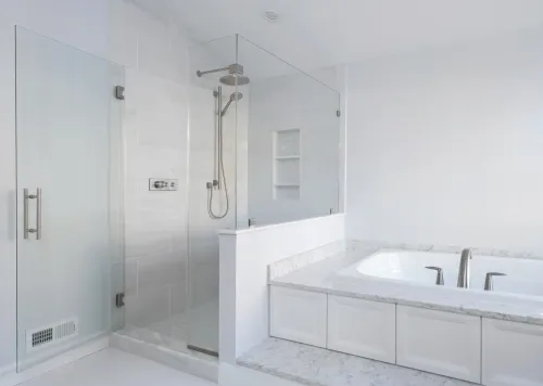 Bright modern bathroom with glass shower and white built-in bathtub in a white tiled room