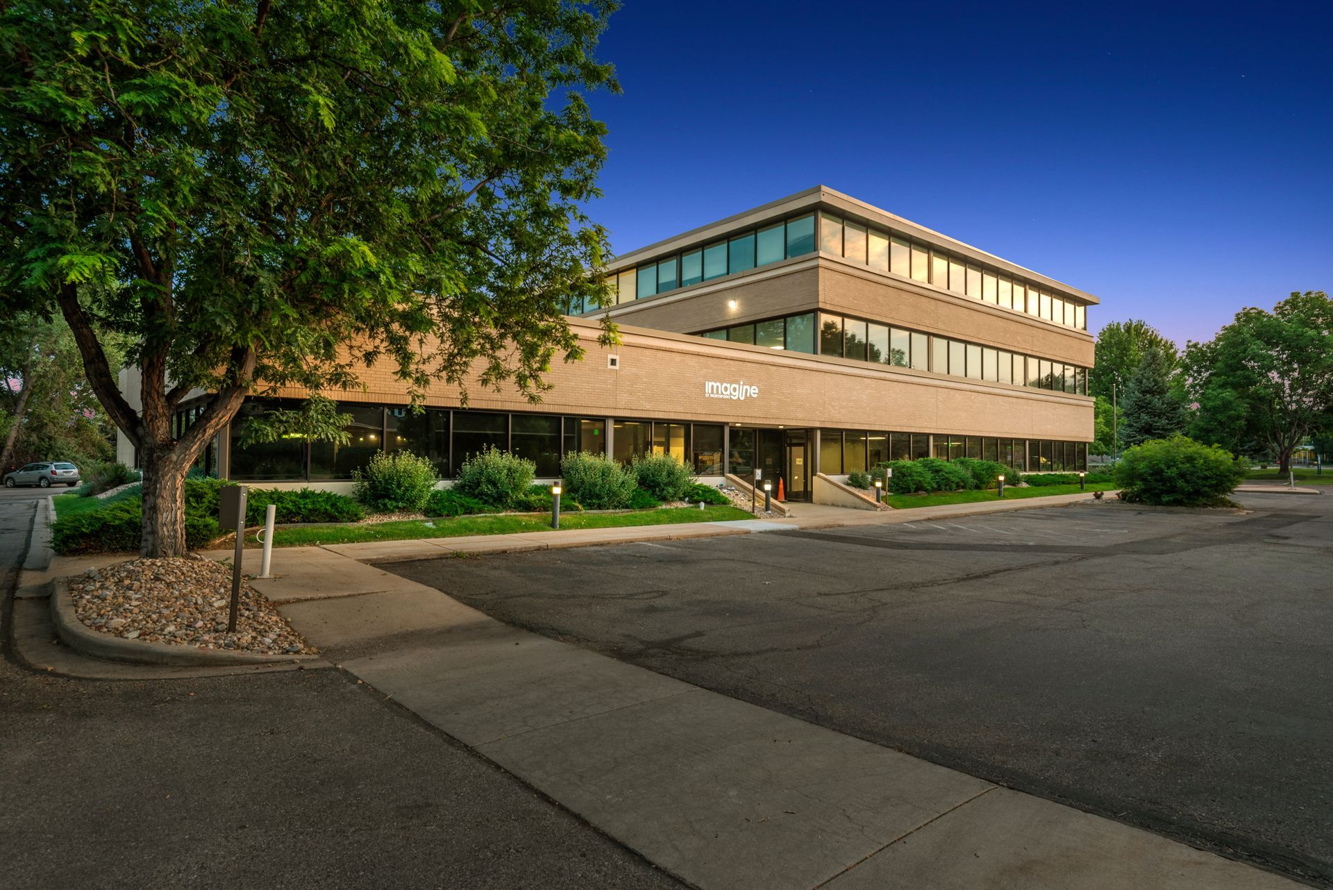 A large building with a lot of windows is surrounded by trees and a parking lot.