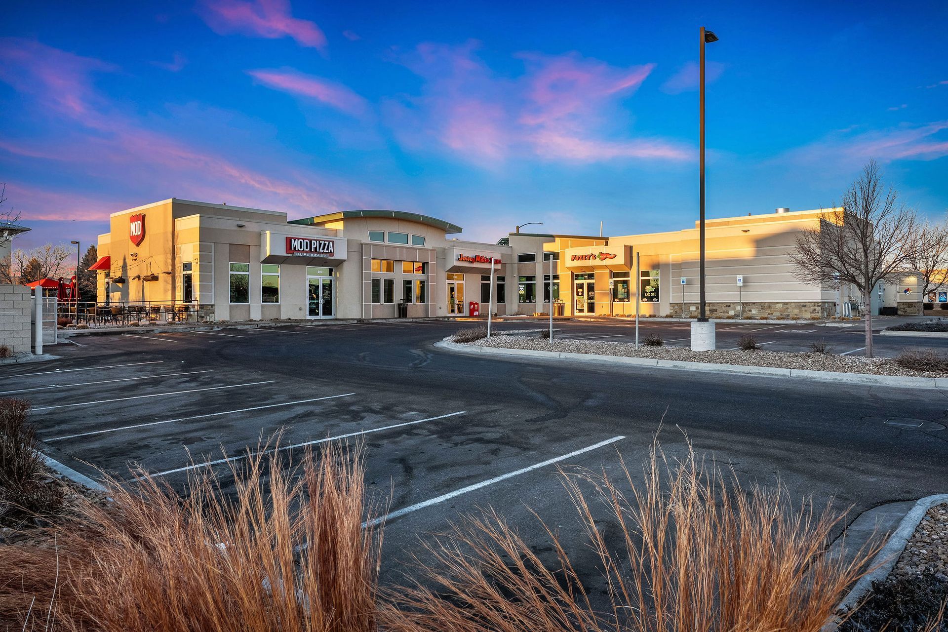 The outside of a burger king restaurant with umbrellas and tables.