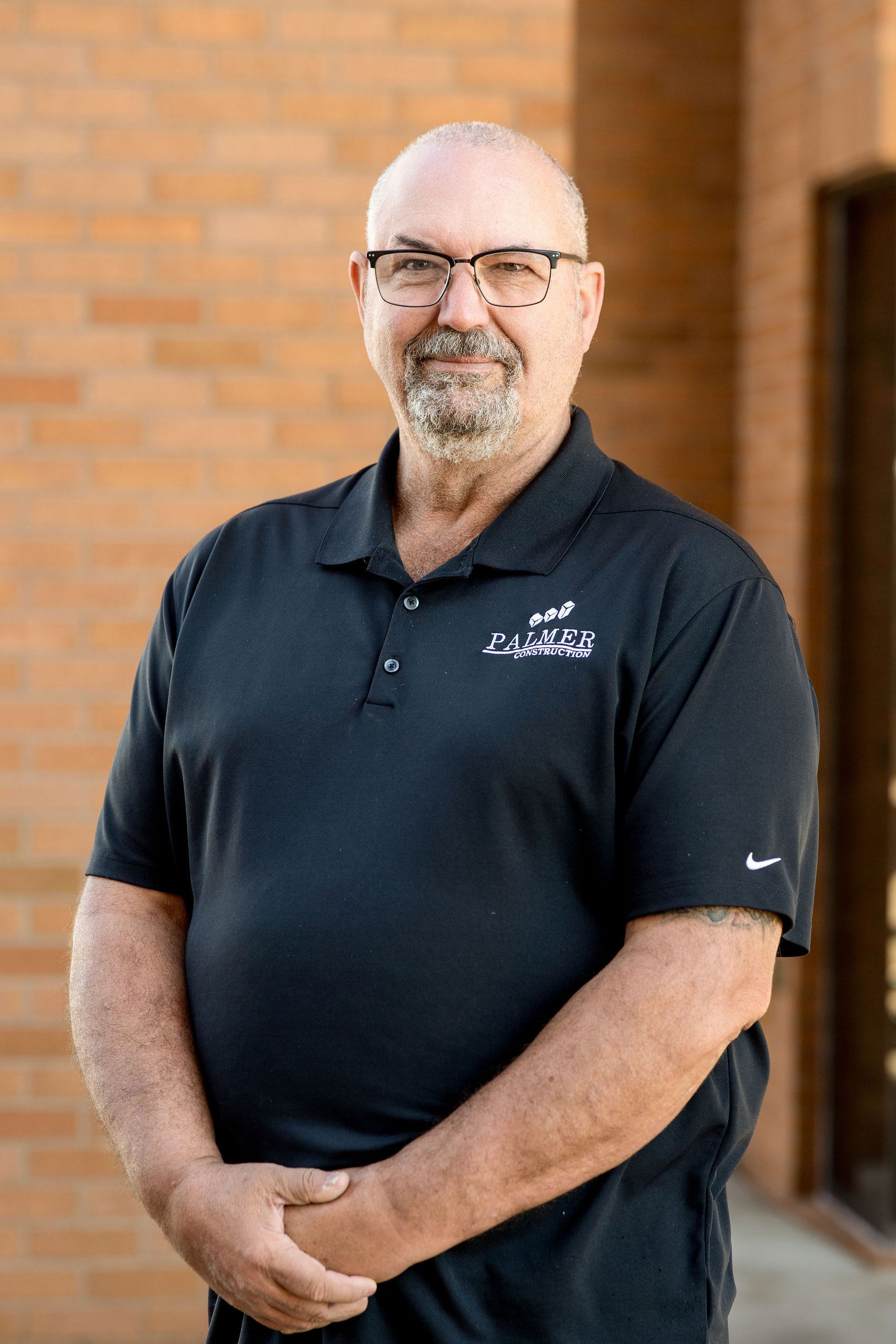A man in a black shirt is smiling in front of a brick building.