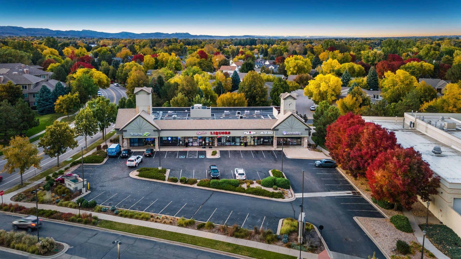 An aerial view of a shopping center surrounded by trees and a parking lot.
