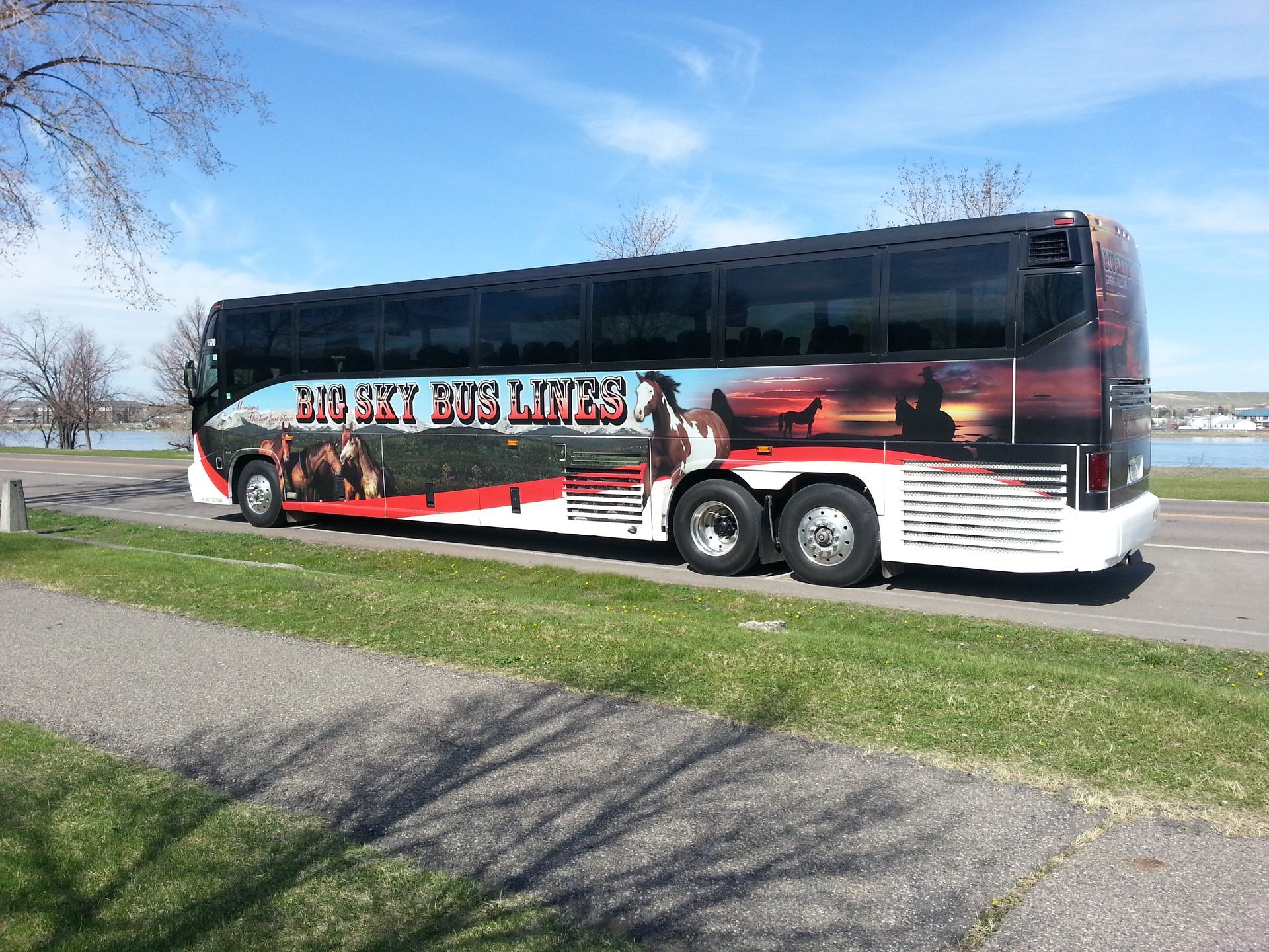 A black-and-red tour bus parked beside a road on a sunny day.