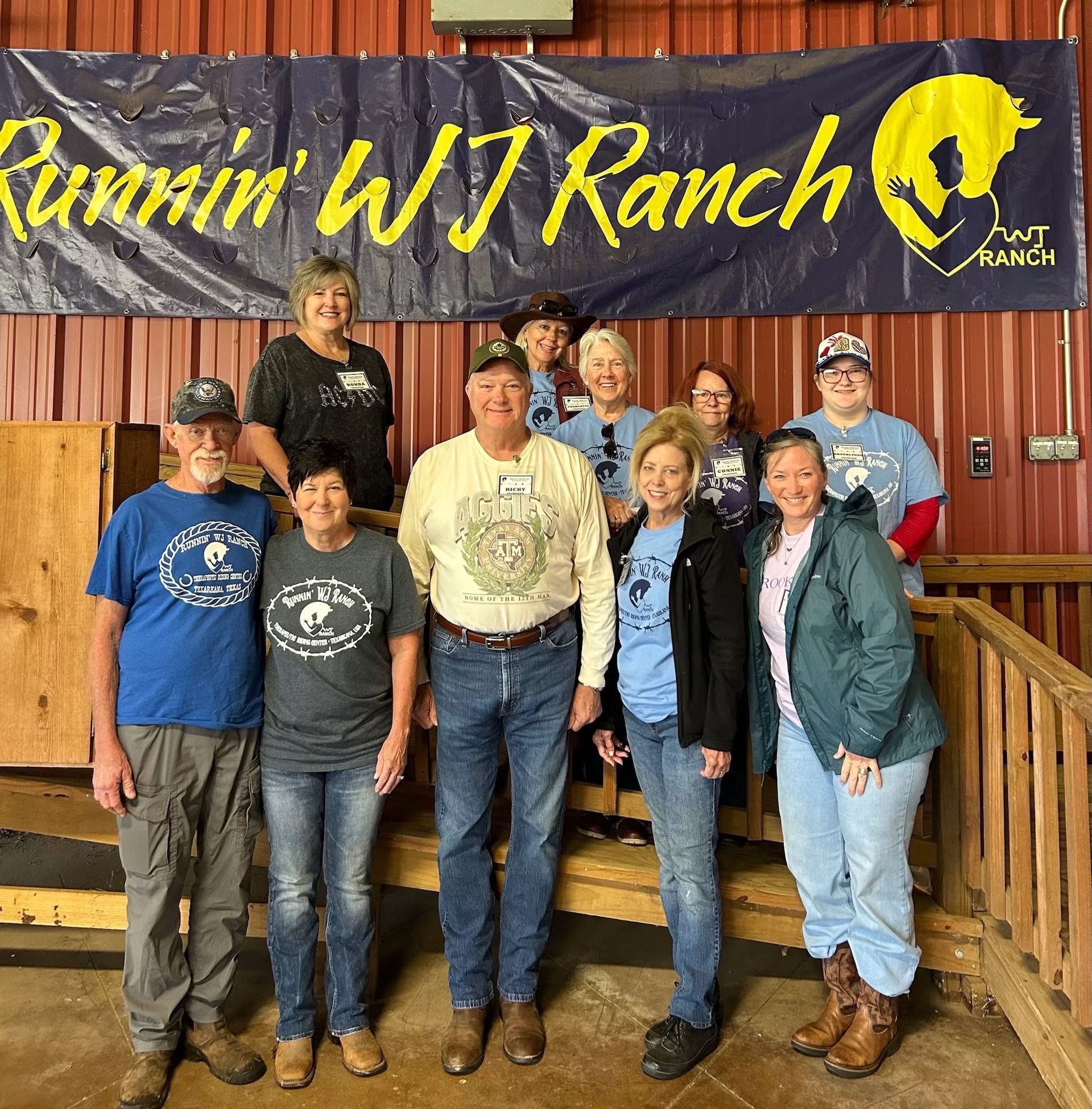 Group posing on a rustic porch under a “Runnin’ W J Ranch” banner, smiling at the camera.