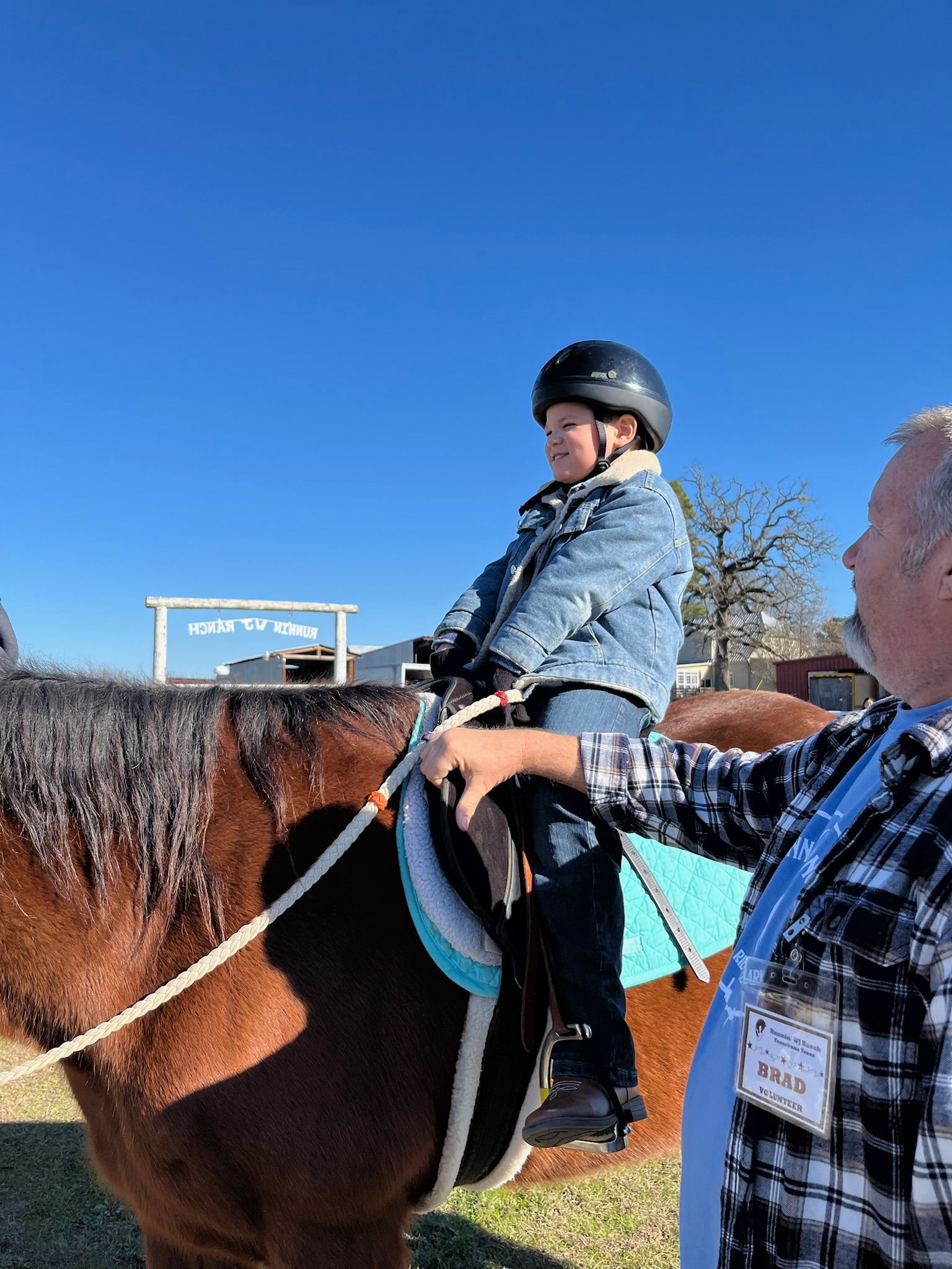 Person riding a brown horse outdoors, with another person holding the reins under a clear blue sky