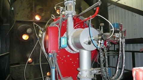 Red and silver industrial boiler with multiple pipes, wires, and gauges.
