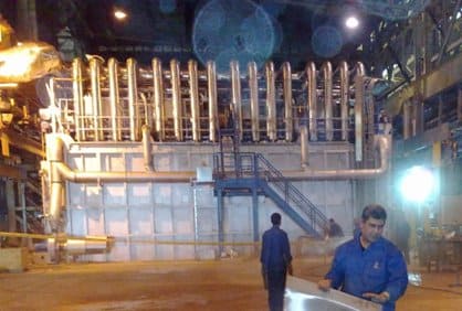 Industrial furnace with pipes, metal sheeting, and workers in a factory setting.