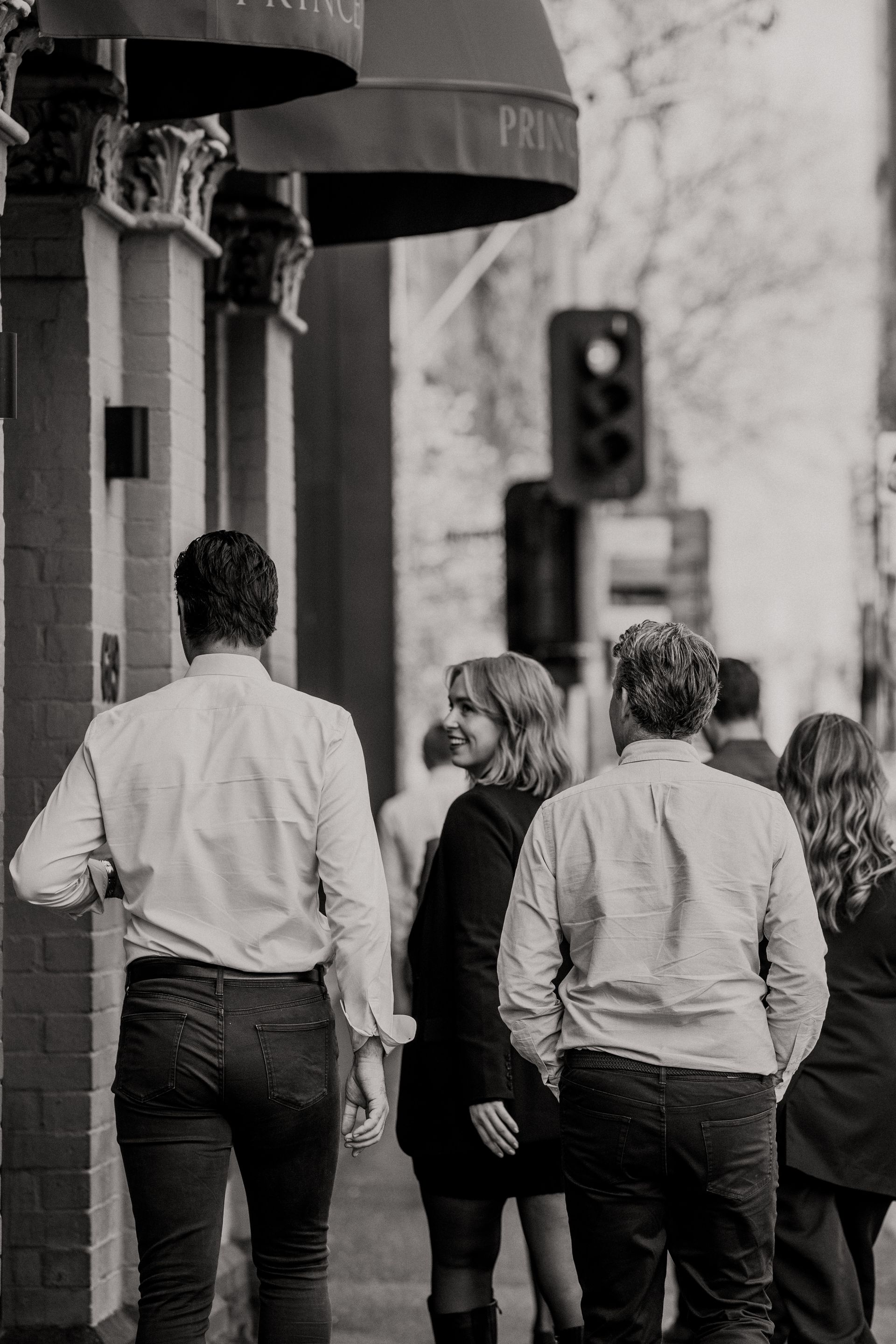 People walking on a city sidewalk past a building with a dark awning.