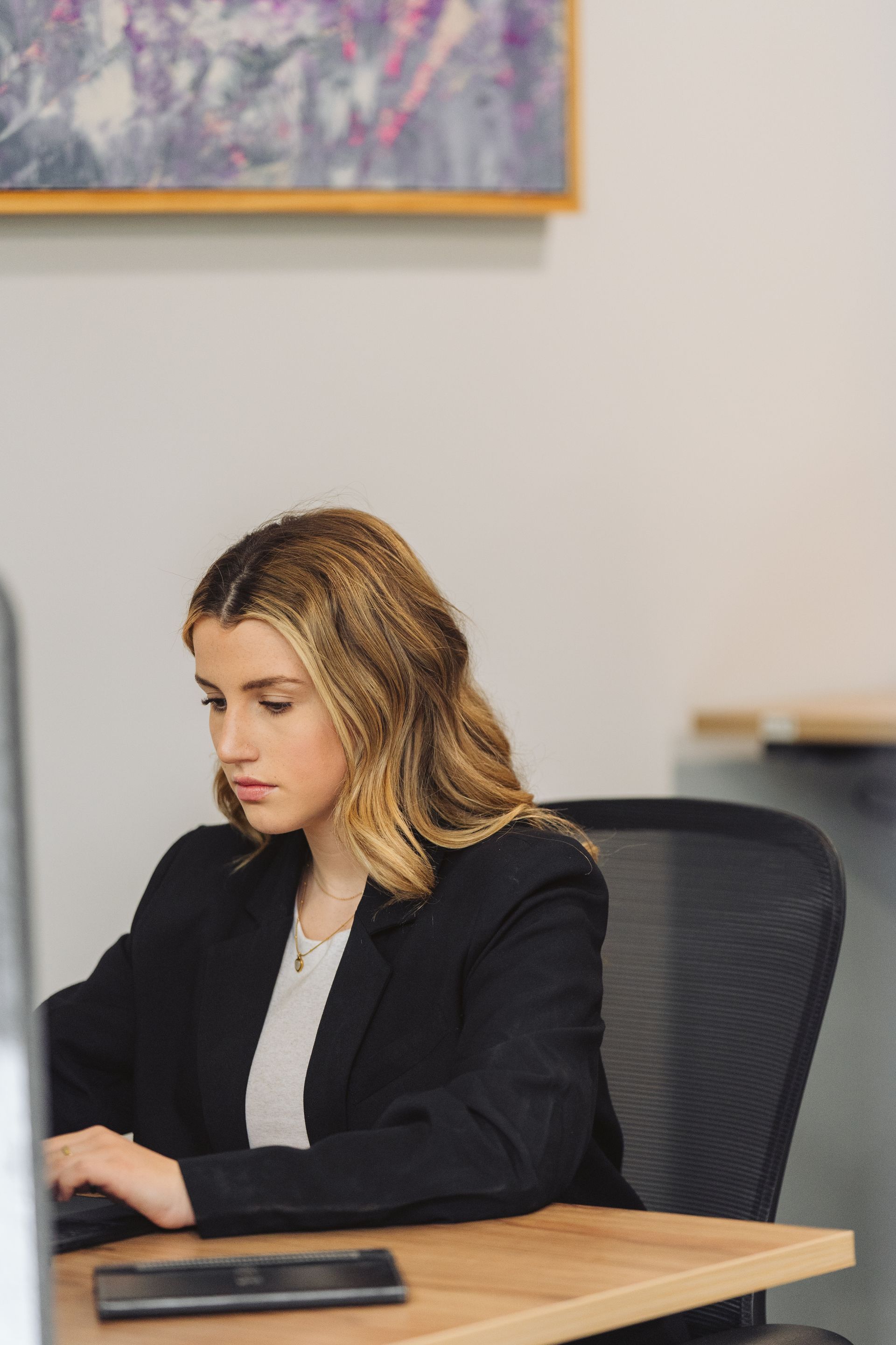 Woman in a blazer working at a desk with a computer.