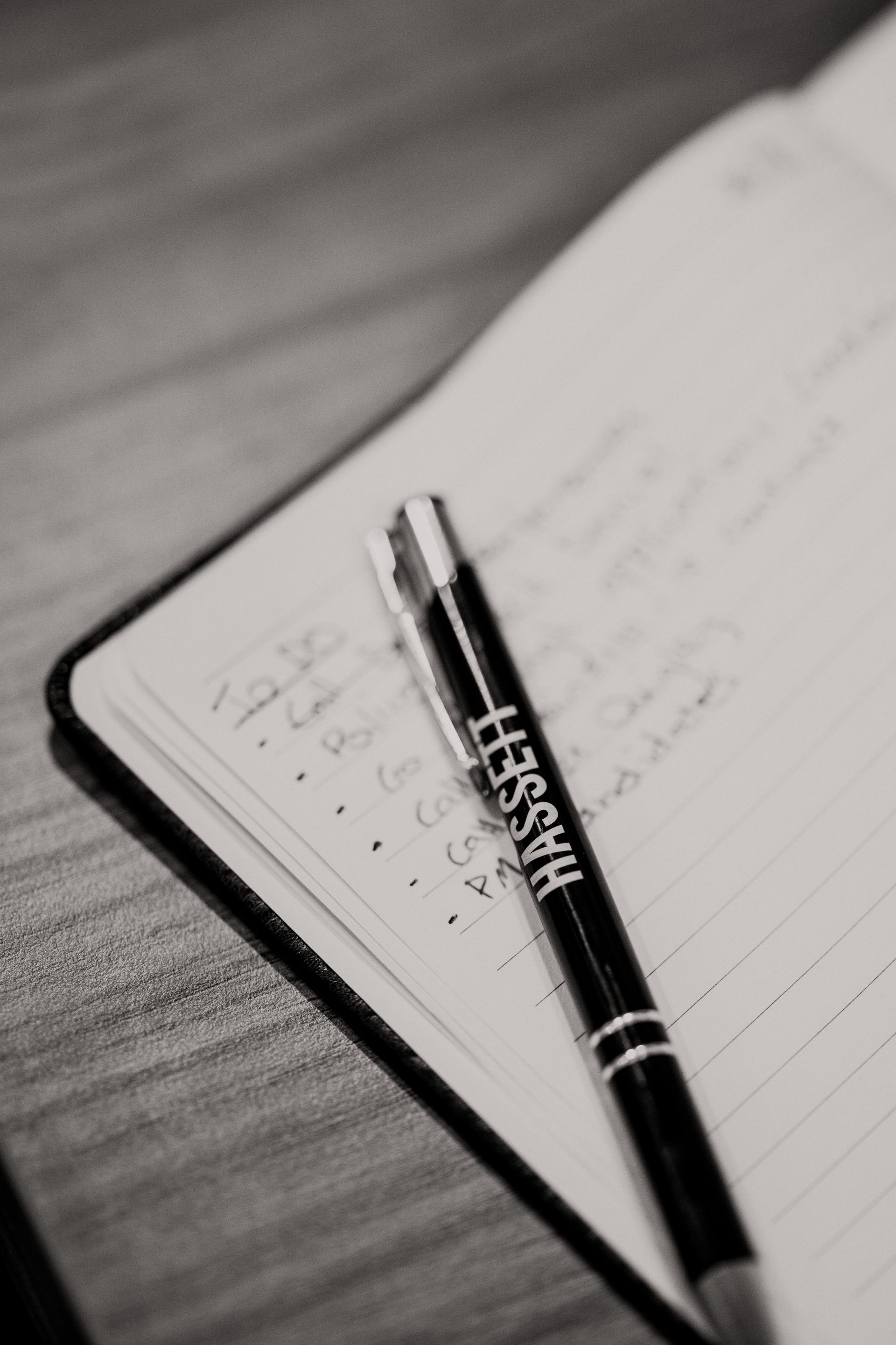 Black and white photo of an open notebook with handwritten notes and a pen with