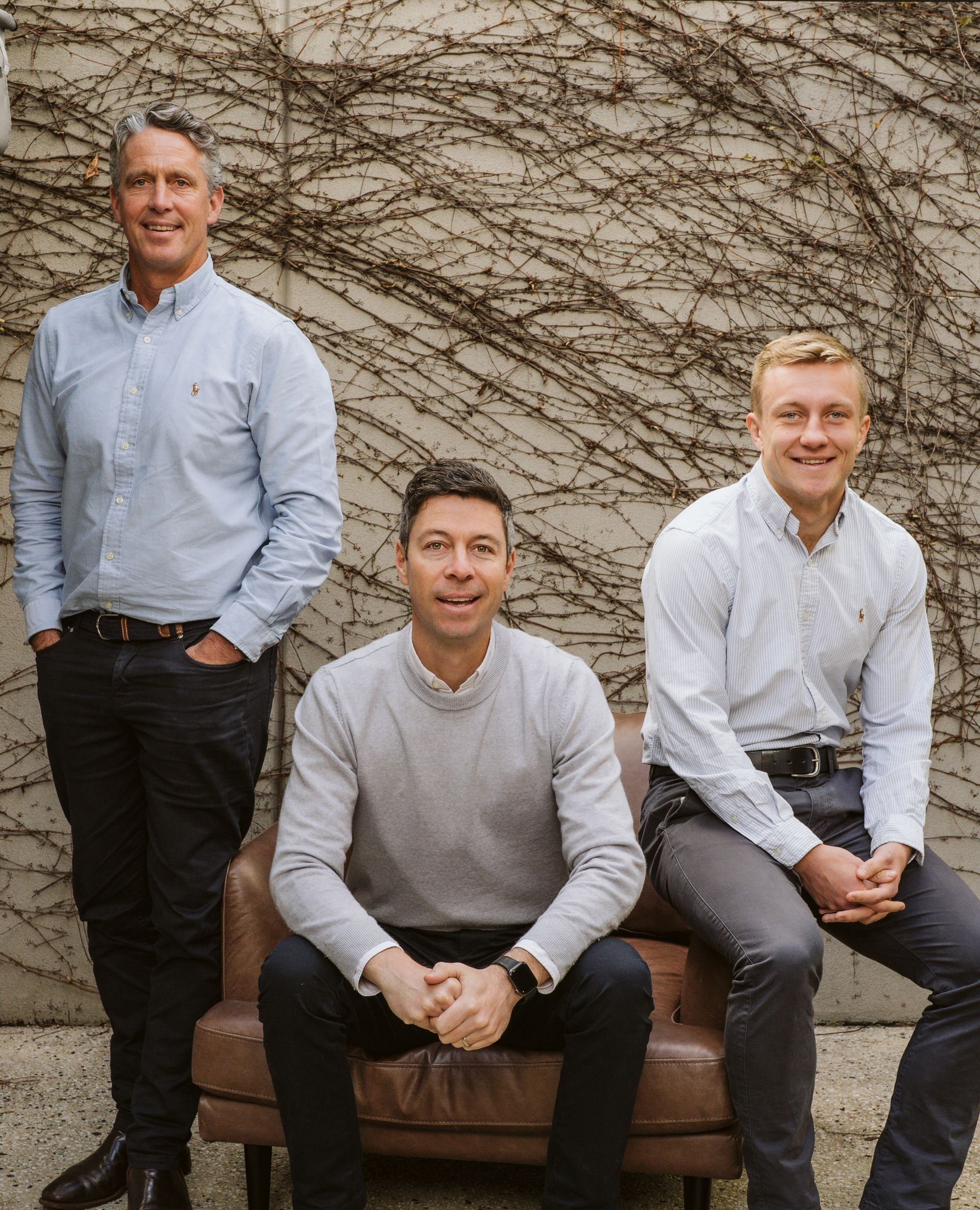 Five people standing in front of a vine-covered wall; three men, two women, smiling.