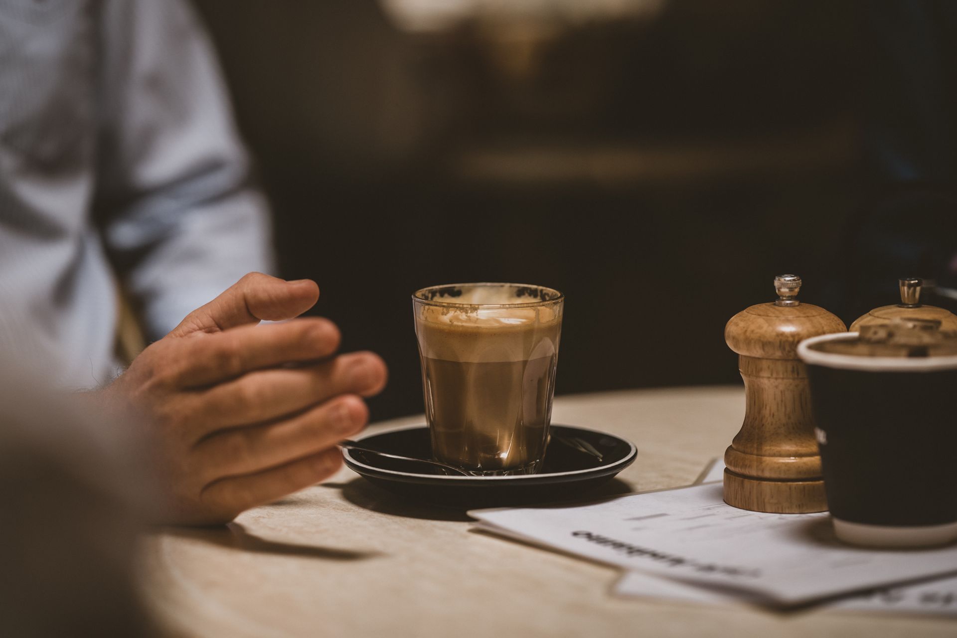 Coffee drink on a saucer, table setting with hand, salt shakers, and a menu.