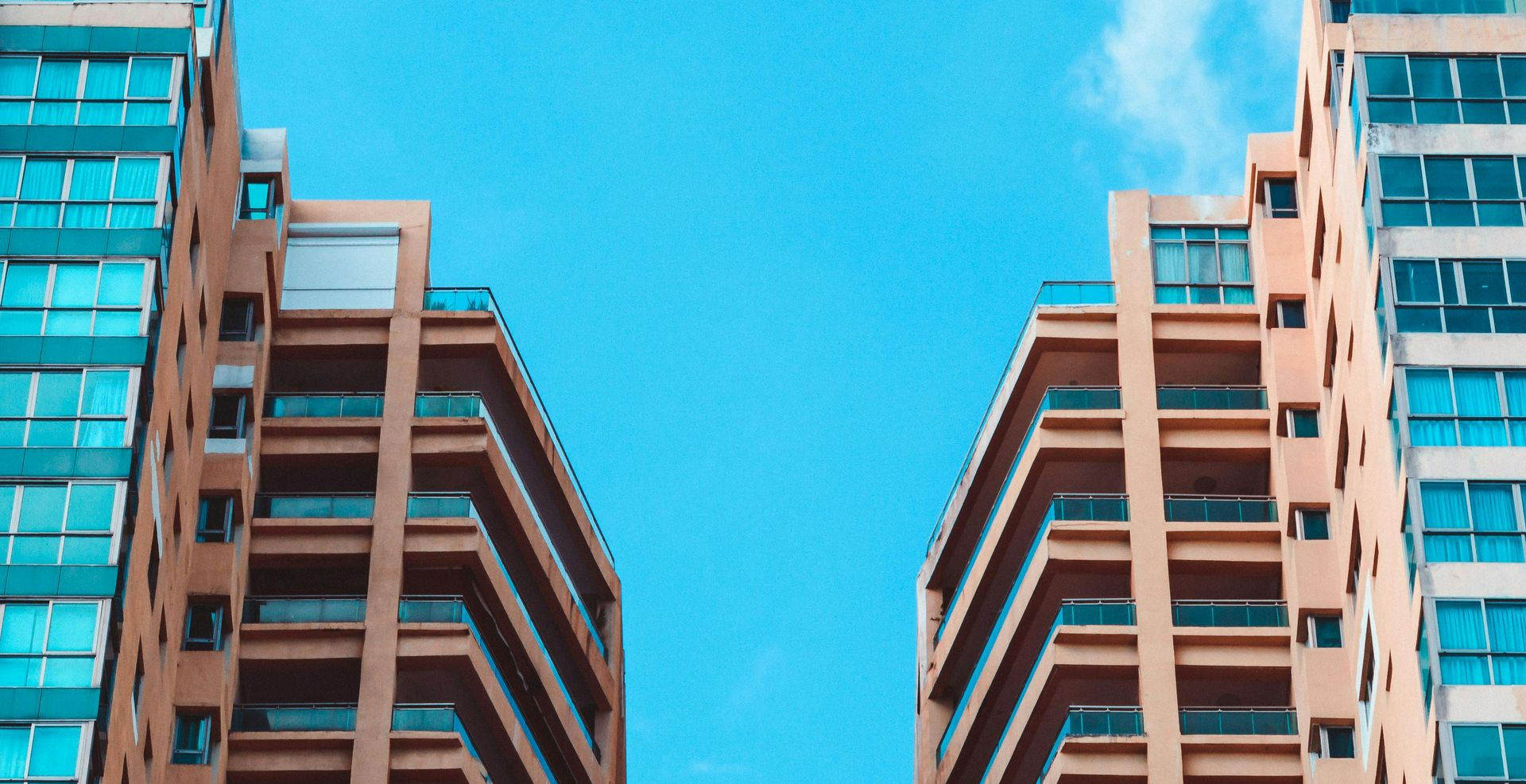 Two tall buildings with multiple balconies against a bright blue sky.