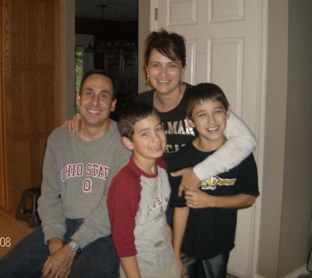 Four smiling people posing indoors in a doorway, with two boys in front and two adults behind them