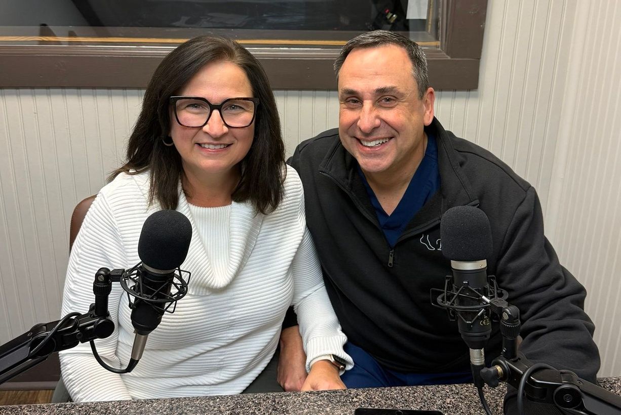 Two hosts smiling at microphones in a podcast studio with soundproof walls.