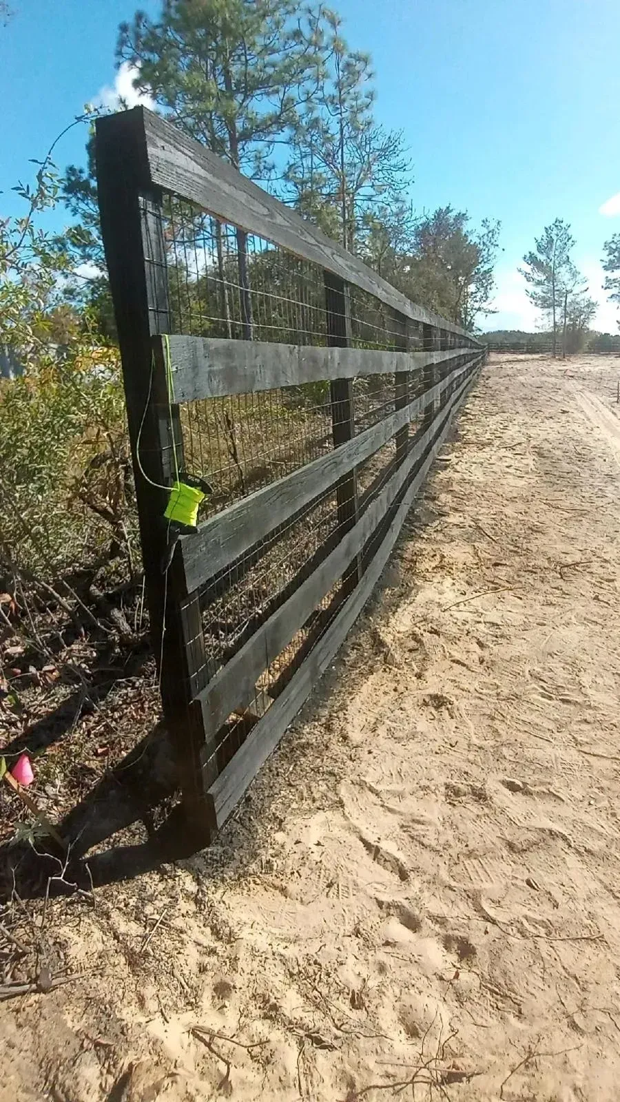 Black wooden fence beside a sandy path under a bright blue sky