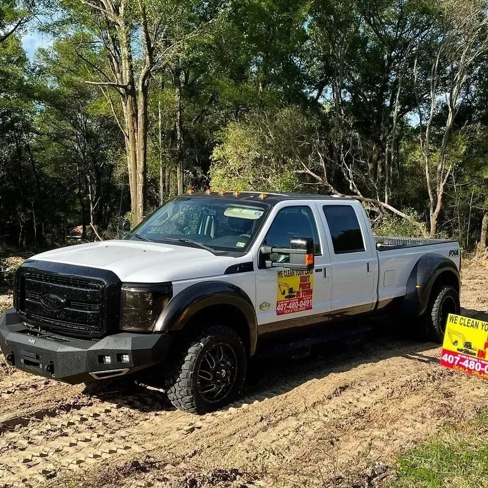 White pickup truck with off-road tires on a muddy trail in a wooded area