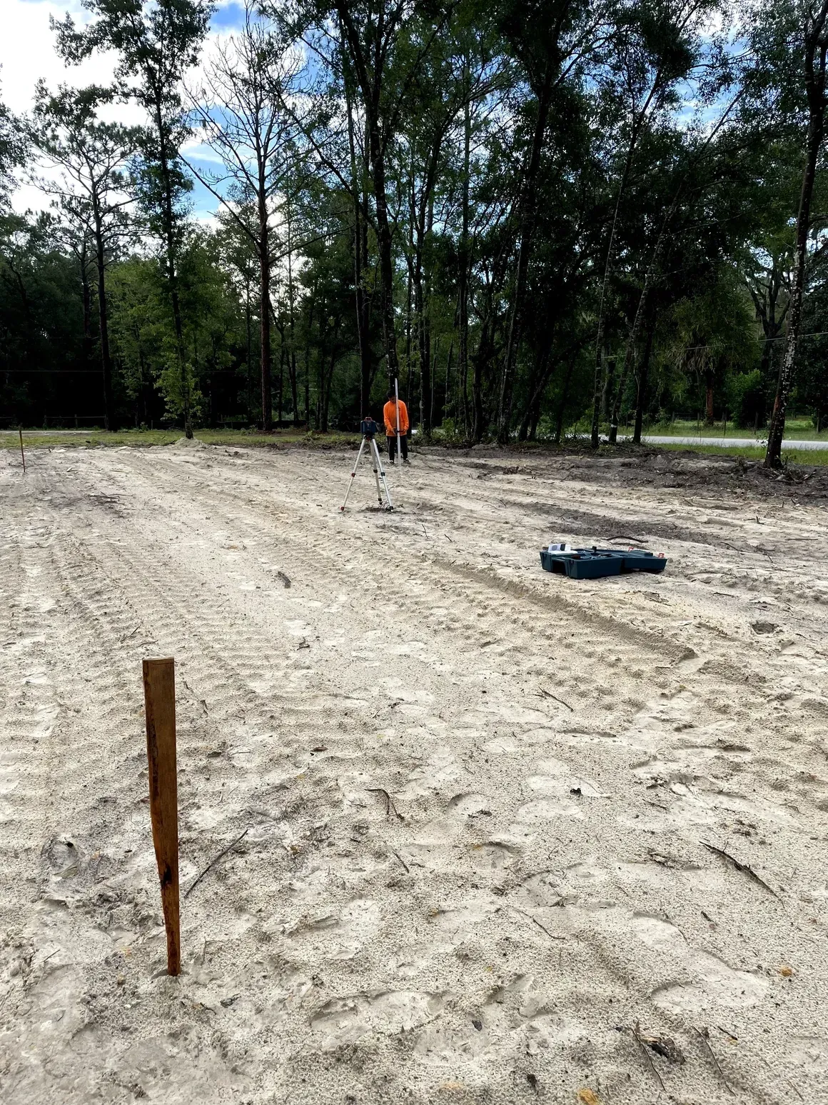 Wooded clearing with a dirt lot, orange marker, and a person standing in the distance
