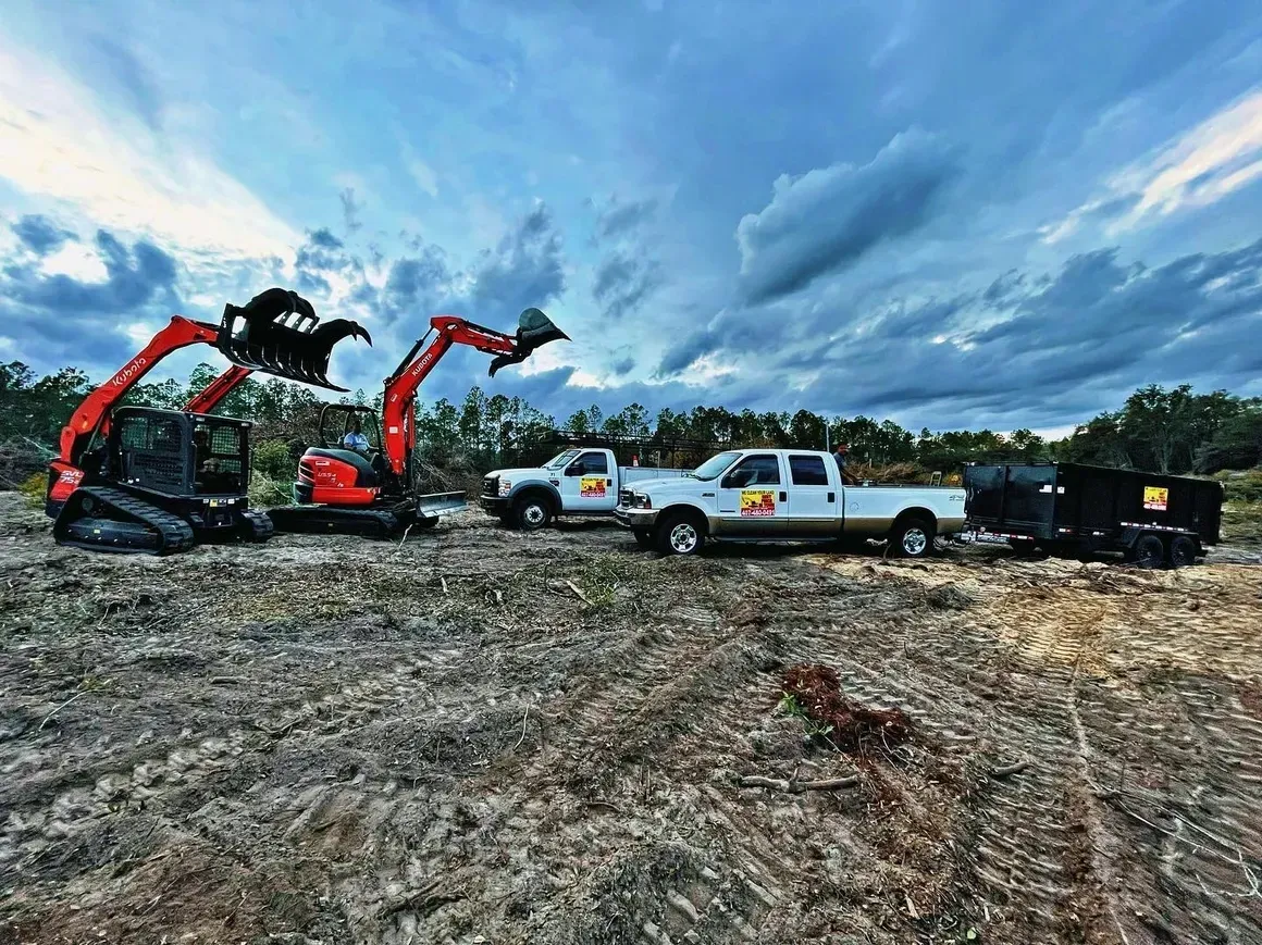 Excavators and pickup trucks on a muddy construction site under a dramatic cloudy sky