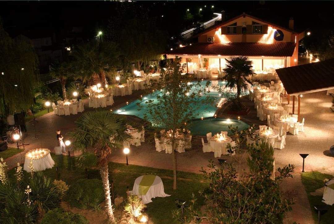 A large swimming pool is surrounded by tables and chairs at night.