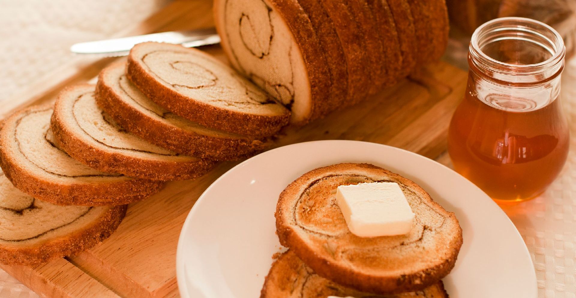 A loaf of bread is sitting on a cutting board next to a plate of toast with butter and syrup.