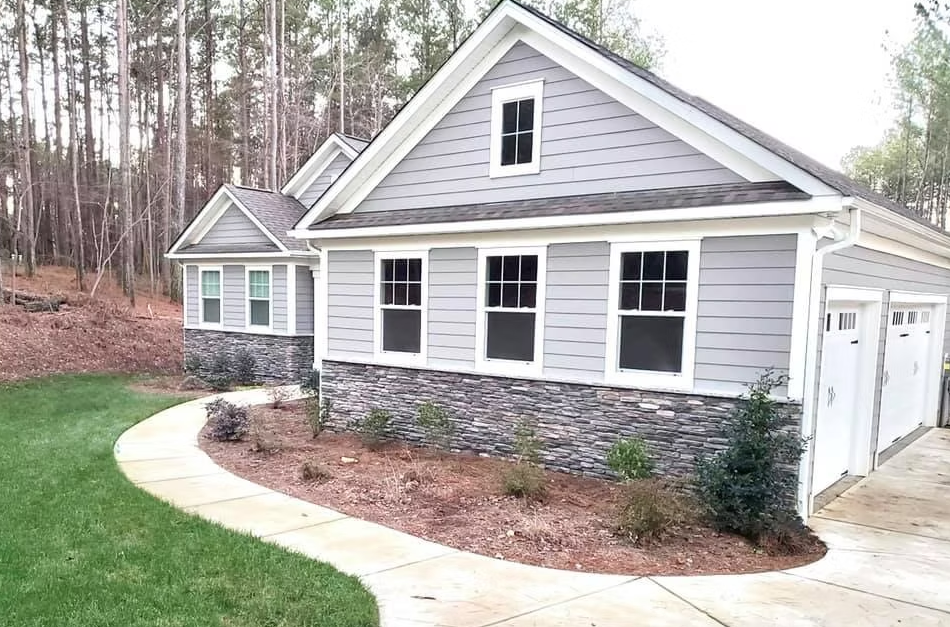 A light gray house with stone foundation, white trim, and a concrete driveway.