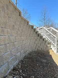 Stone retaining wall with built-in steps leading to a wooden deck, under a bright blue sky.
