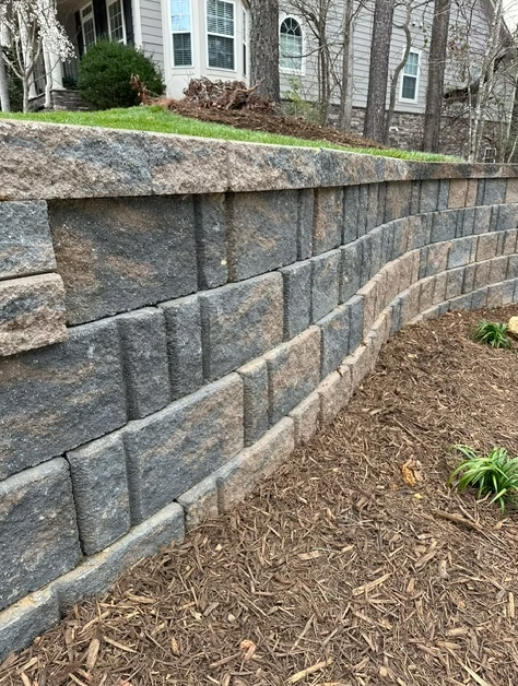 Stone retaining wall with a curved section holding back a grassy hillside.