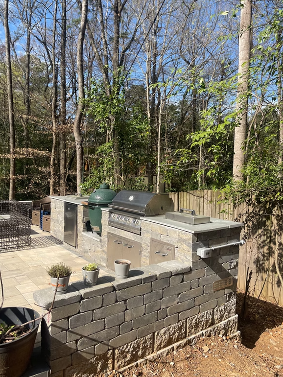 Outdoor kitchen with stone counters, a grill, Big Green Egg, and built-in storage.
