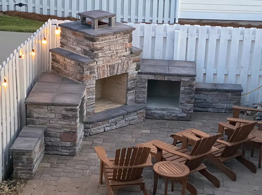 Outdoor patio with stone fireplace, seating area, and wooden chairs.