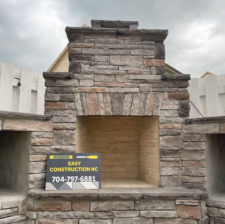 Outdoor stone fireplace constructed by Easy Construction NC, with phone number on sign.