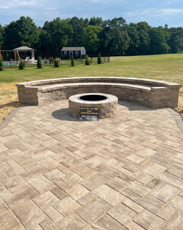 Stone patio with a fire pit and curved seating in a grassy yard.
