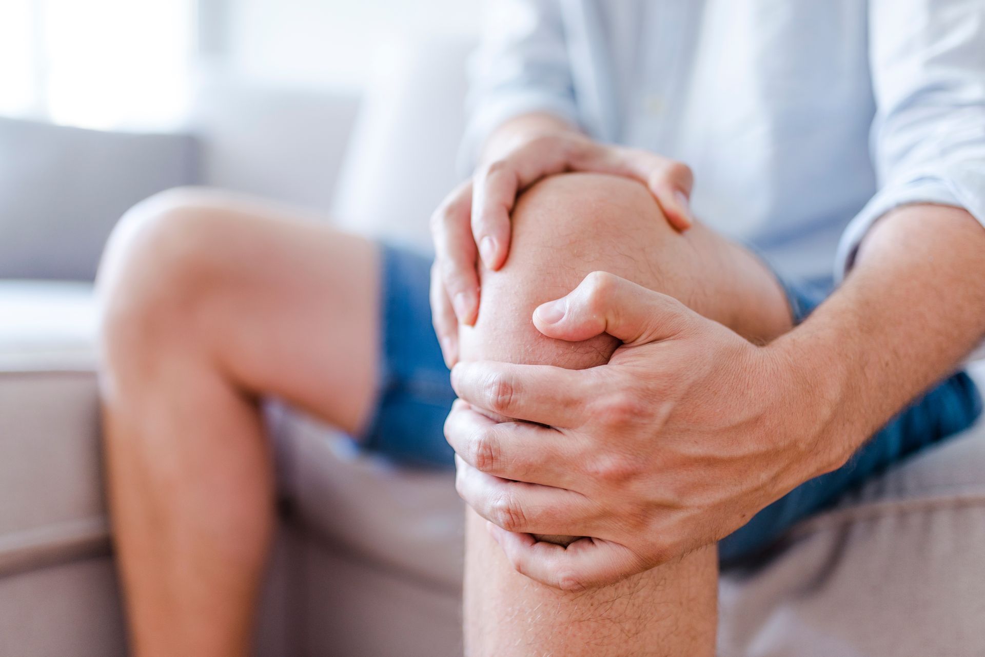 Person seated, holding knee in pain, indoors.
